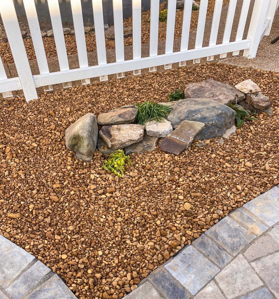 Stone bed under white picket fence